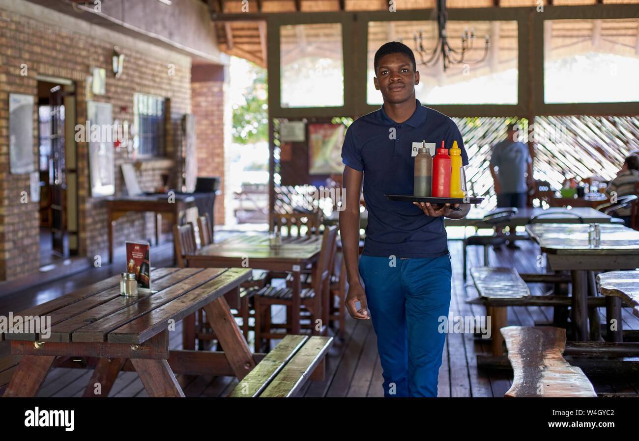 Young waiter serving sauces in bottles in a restaurant, South Africa Stock Photo