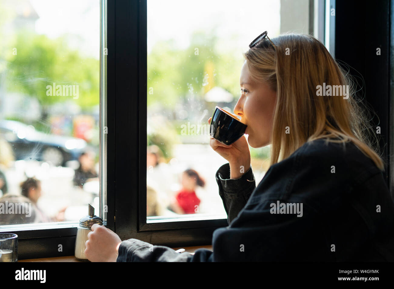 Young woman drinking coffee in a coffee shop looking out of window ...