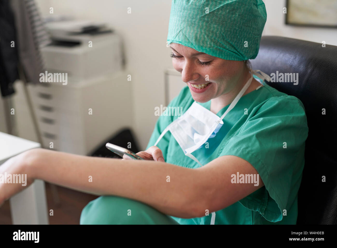 Happy woman in scrubs having a break using cell phone Stock Photo