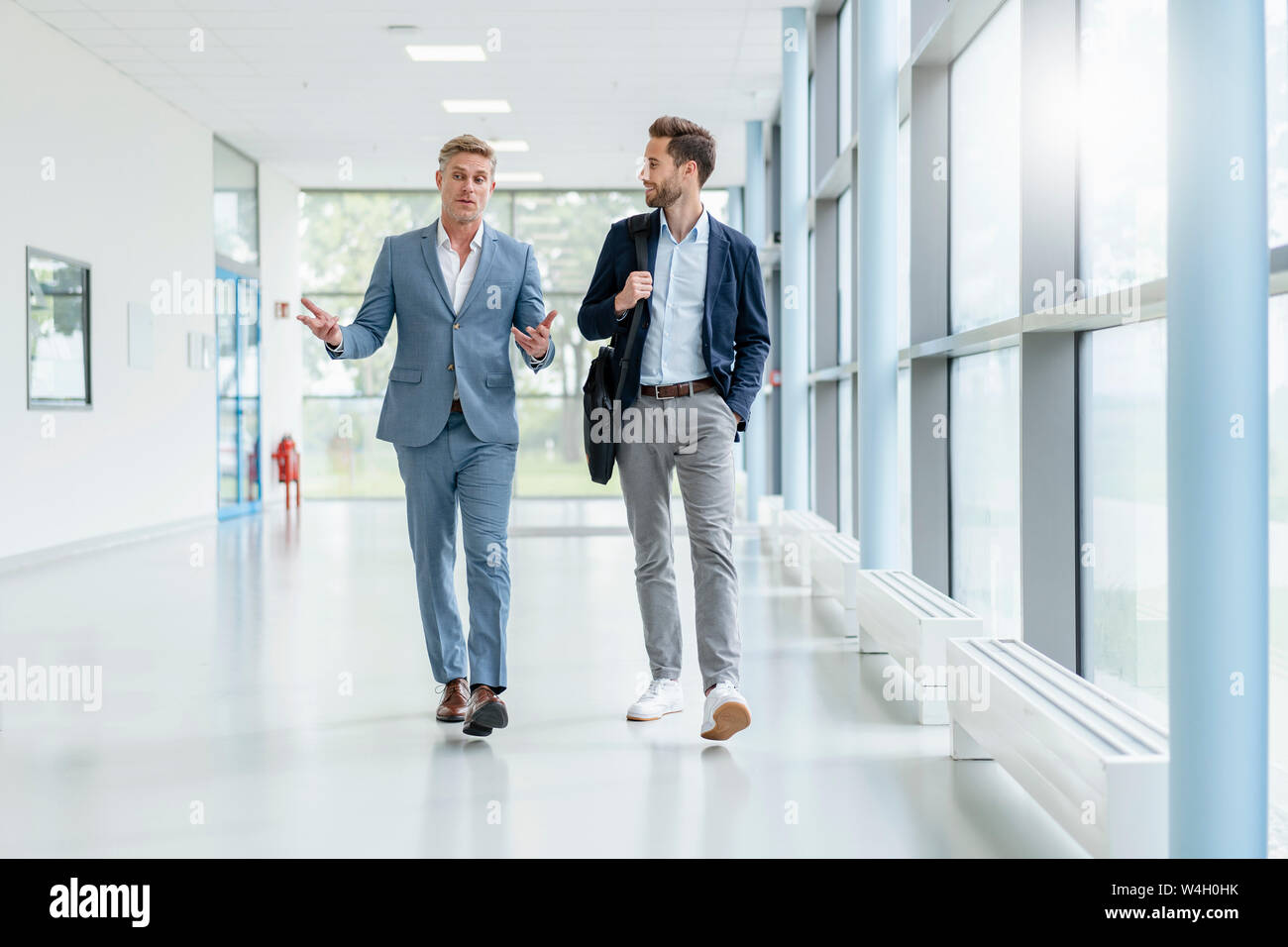 Two businessmen walking and talking in a passageway Stock Photo - Alamy