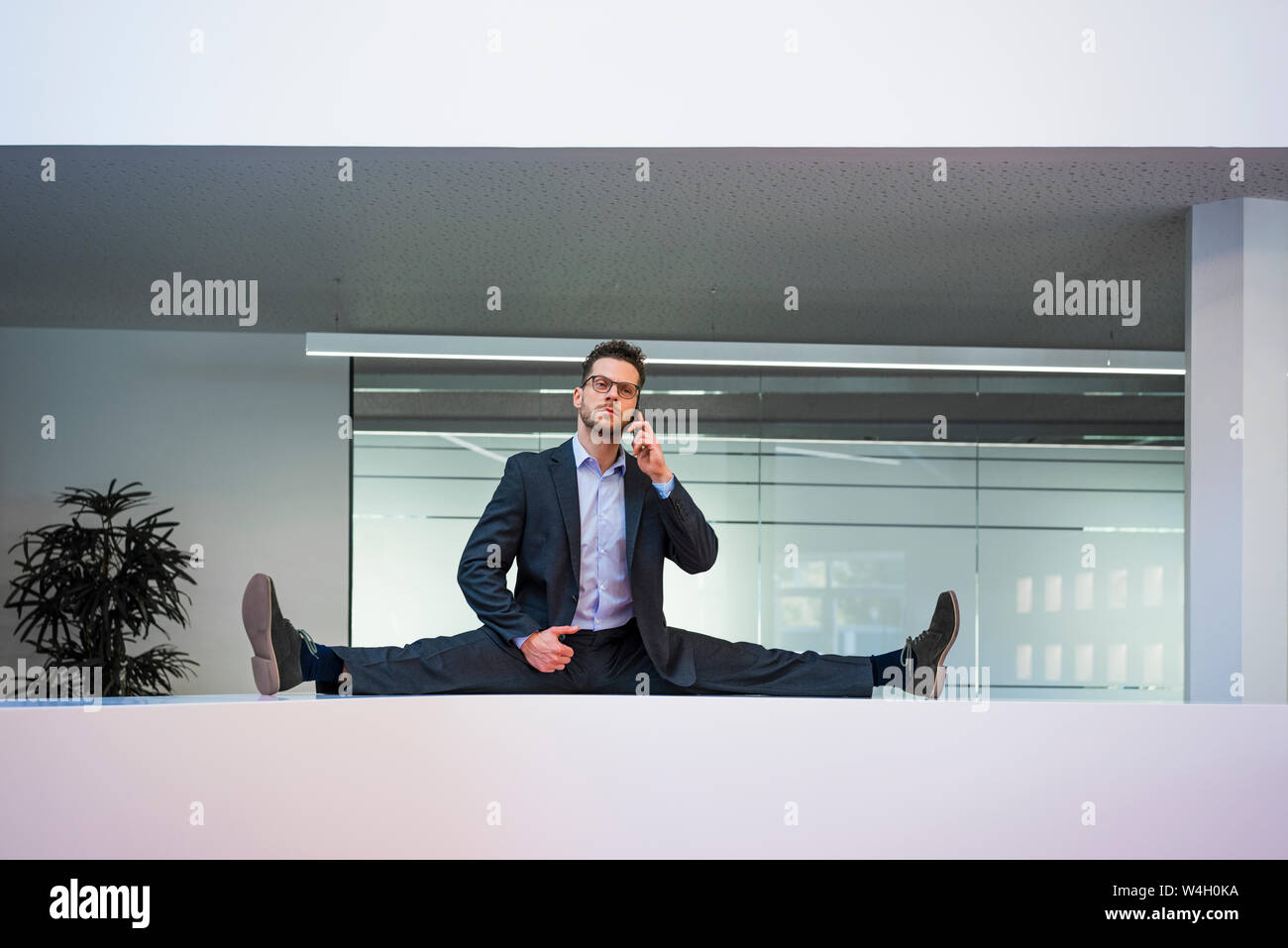 Businessman doing the splits on reception desk in office talking on cell phone Stock Photo