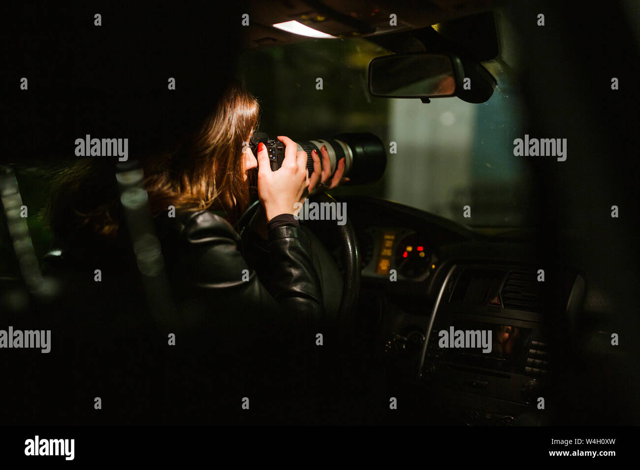Young woman taking pictures with a camera out of a car at night Stock Photo