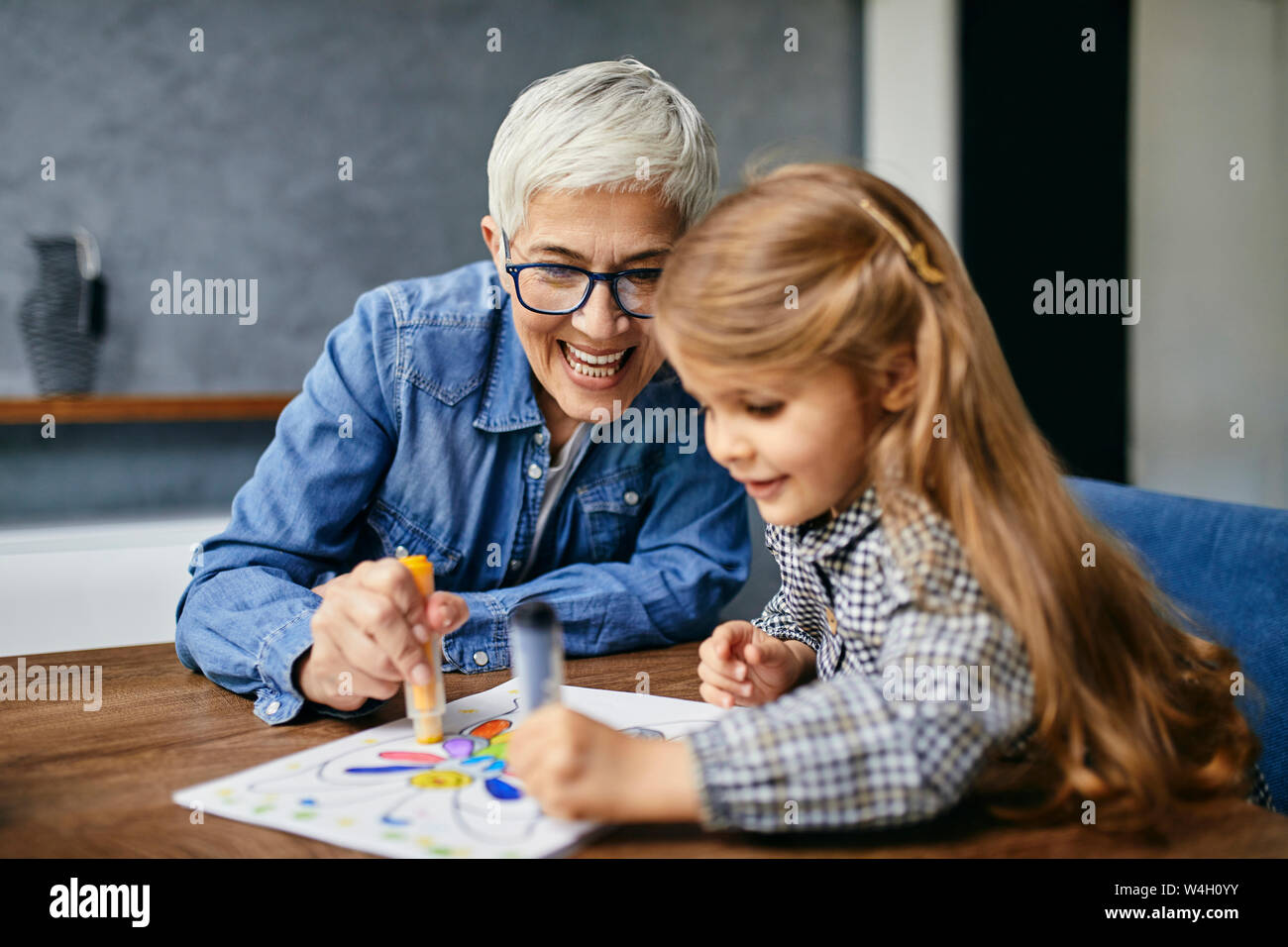 Grandmother and granddaughter sitting at table, painting colouring book Stock Photo