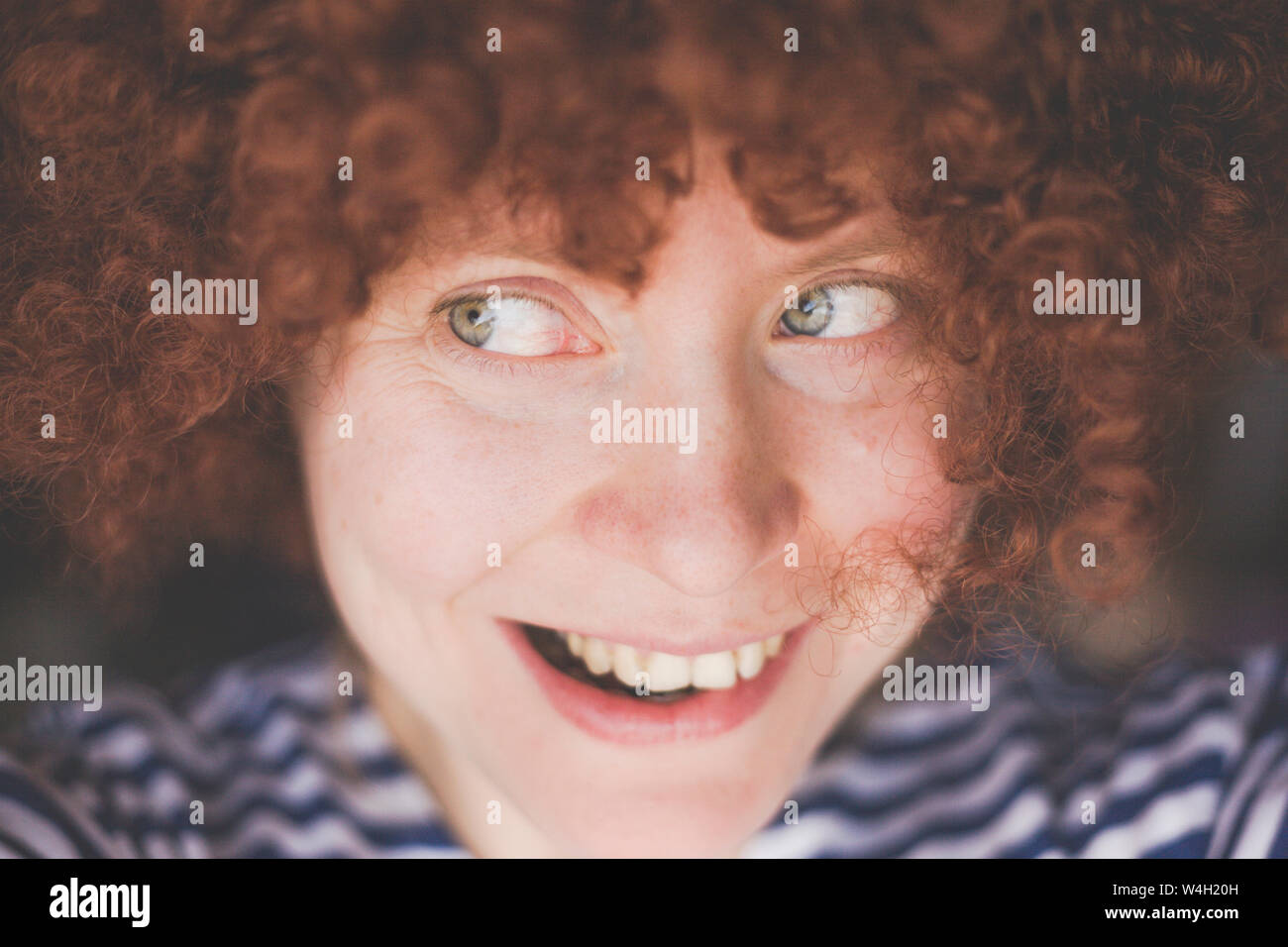 Portrait of smiling woman wearing a red curly carnival wig Stock Photo