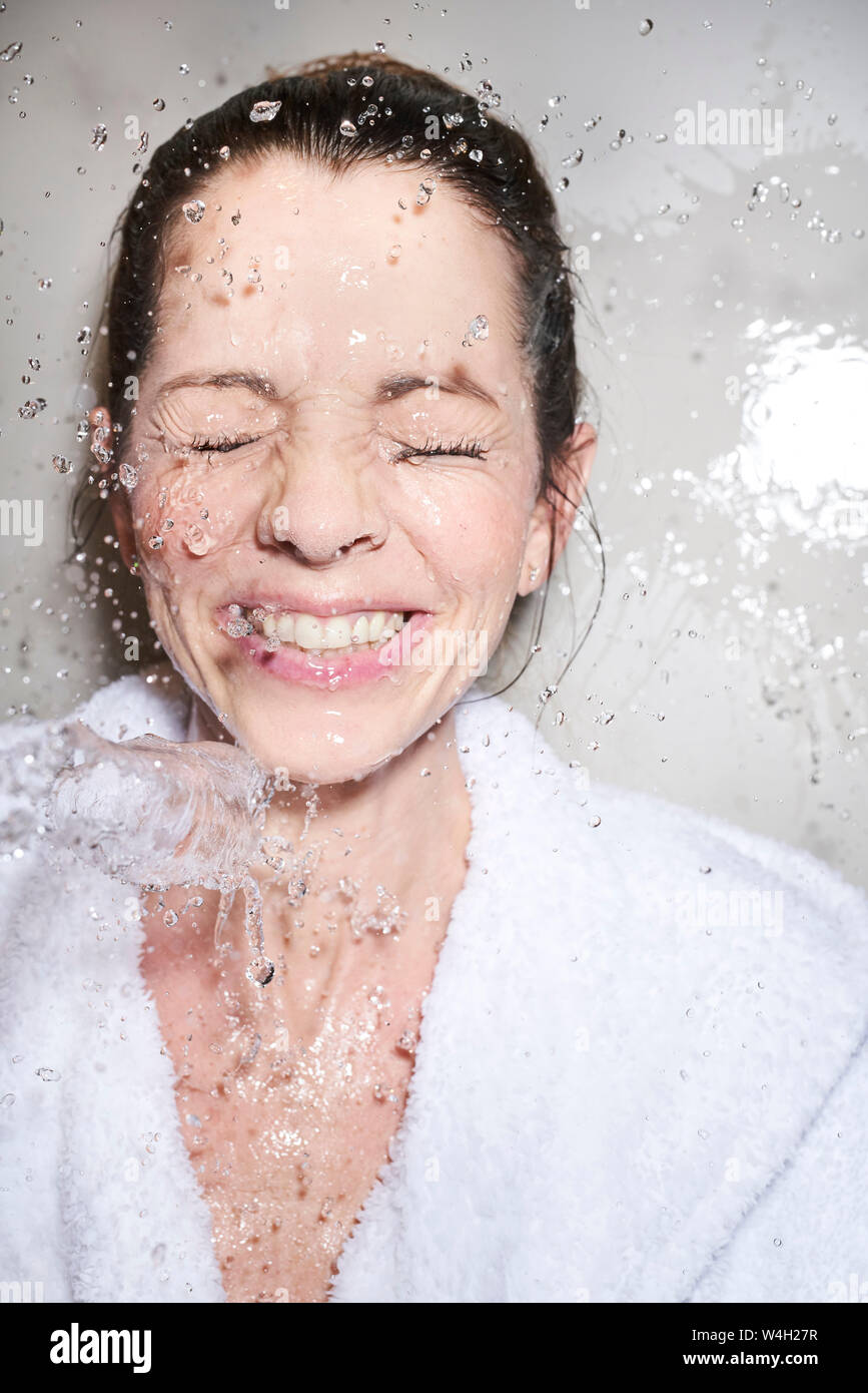 Water splashing into face of happy woman in bathrobe Stock Photo
