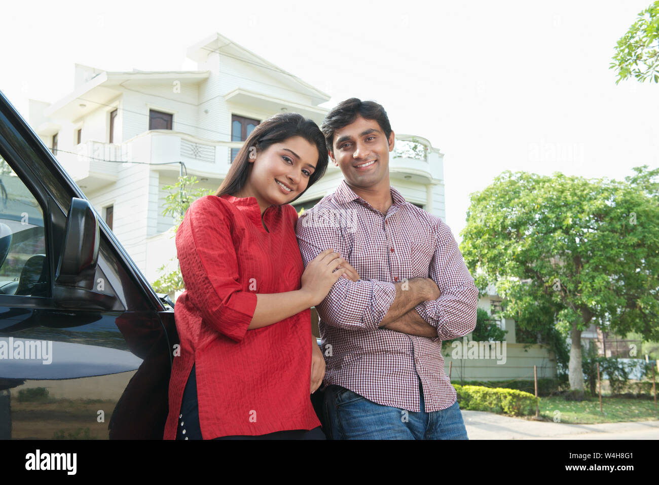 Couple leaning against a car and smiling Stock Photo - Alamy