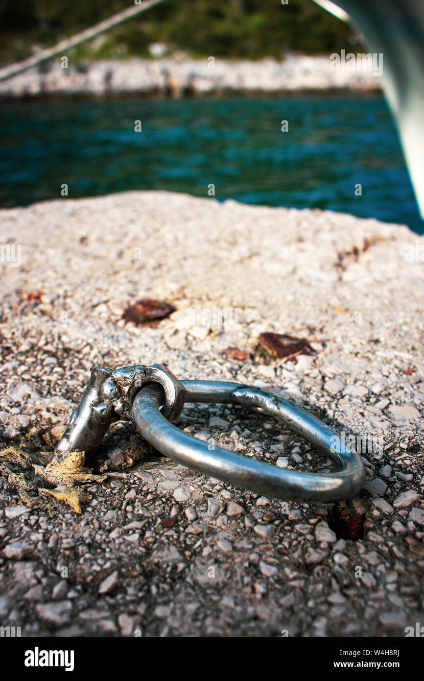 Crazy crafted silver metal mooring ring nailed in the concrete on the shore Stock Photo