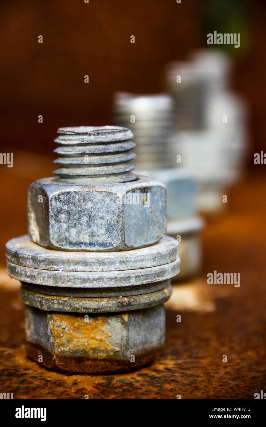 Four silver screws on red rusty metal plate holding construction together Stock Photo