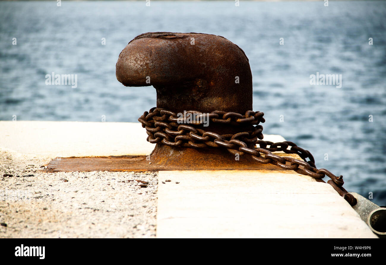 Old and rusty mooring post on concrete dock of harbor Stock Photo