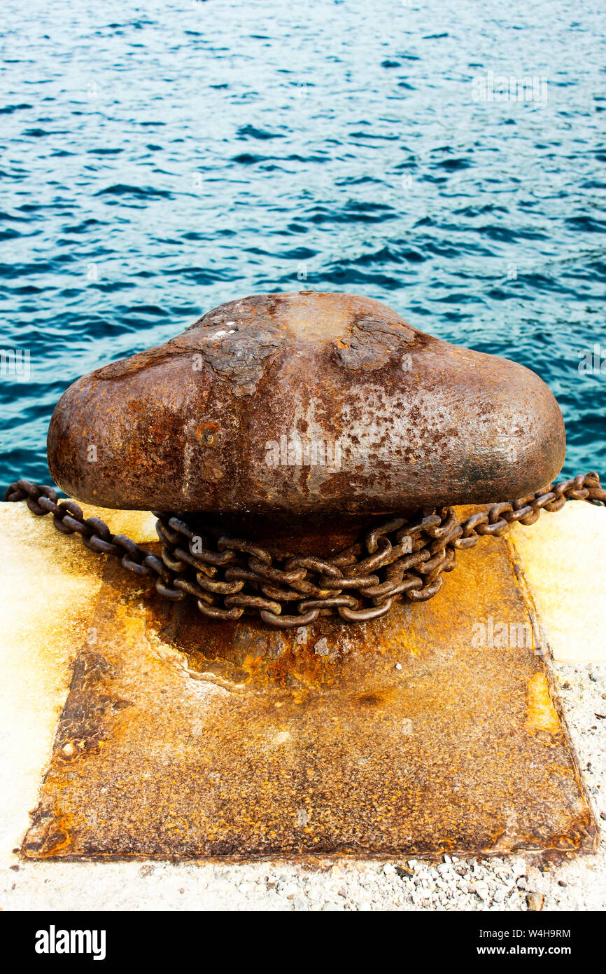 Old and rusty mooring post on concrete dock of harbor Stock Photo