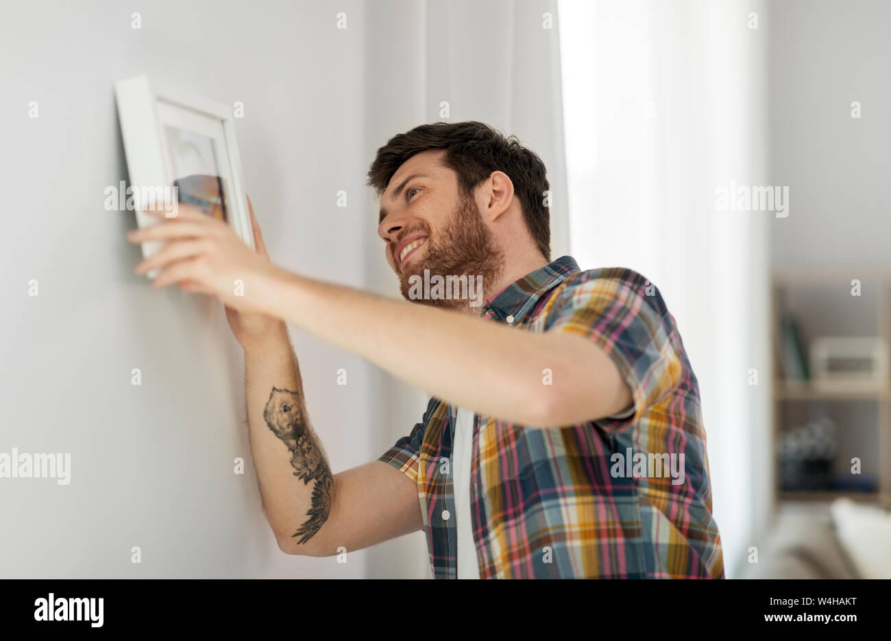 man hanging picture in frame to wall at home Stock Photo