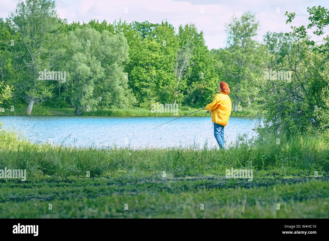 Woman in yellow jacket fishing spinning on lake Stock Photo - Alamy