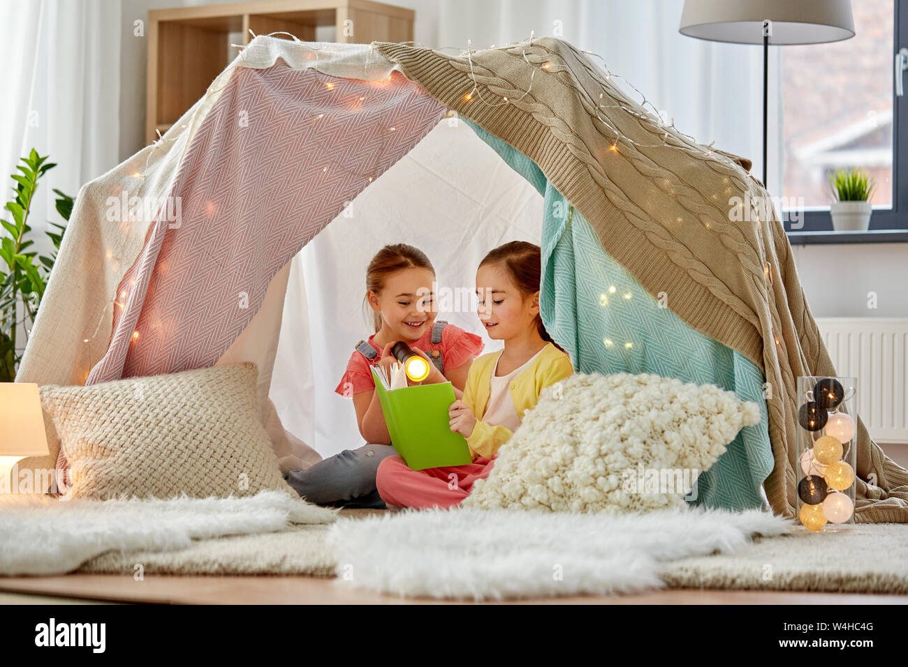 happy girls reading book in kids tent at home Stock Photo - Alamy