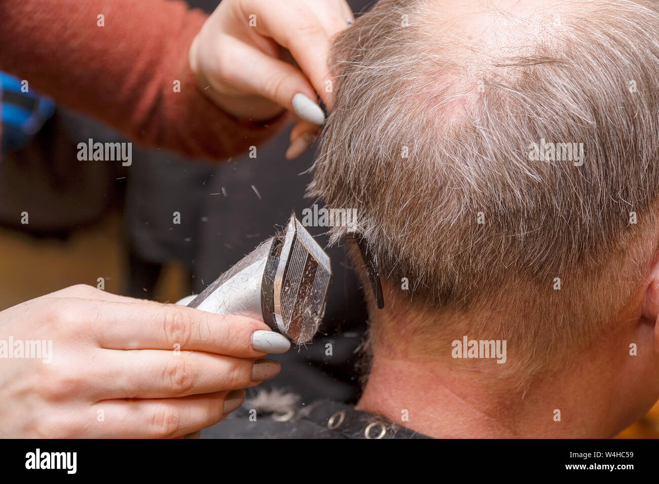 Woman Hairdresser cuts man's hair with electric clipper trimmer Stock