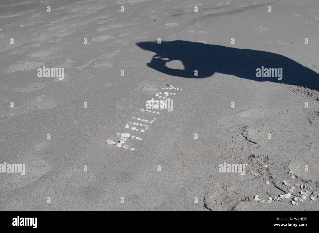 Inscription made of shells on sand and shadow photographing tourists ...