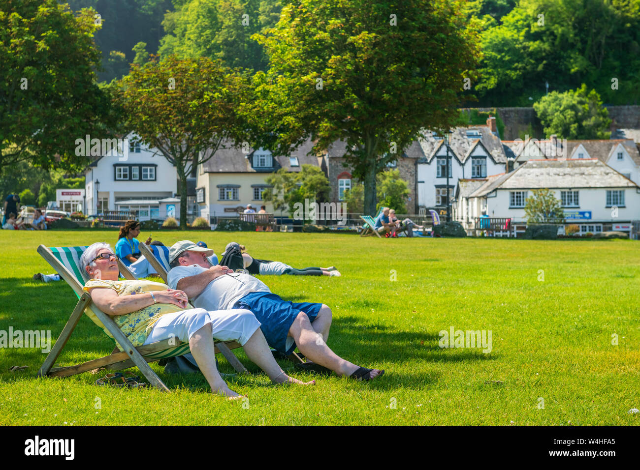 Lynmouth Harbour, North Devon, England. Tuesday 23rd July 2019. UK Weather.  With temperatures soaring under blue skies, holidaymakers enjoy soaking up the sunshine in the little park next to the picturesque harbour at Lynmouth in North Devon. Credit: Terry Mathews/Alamy Live News Stock Photo