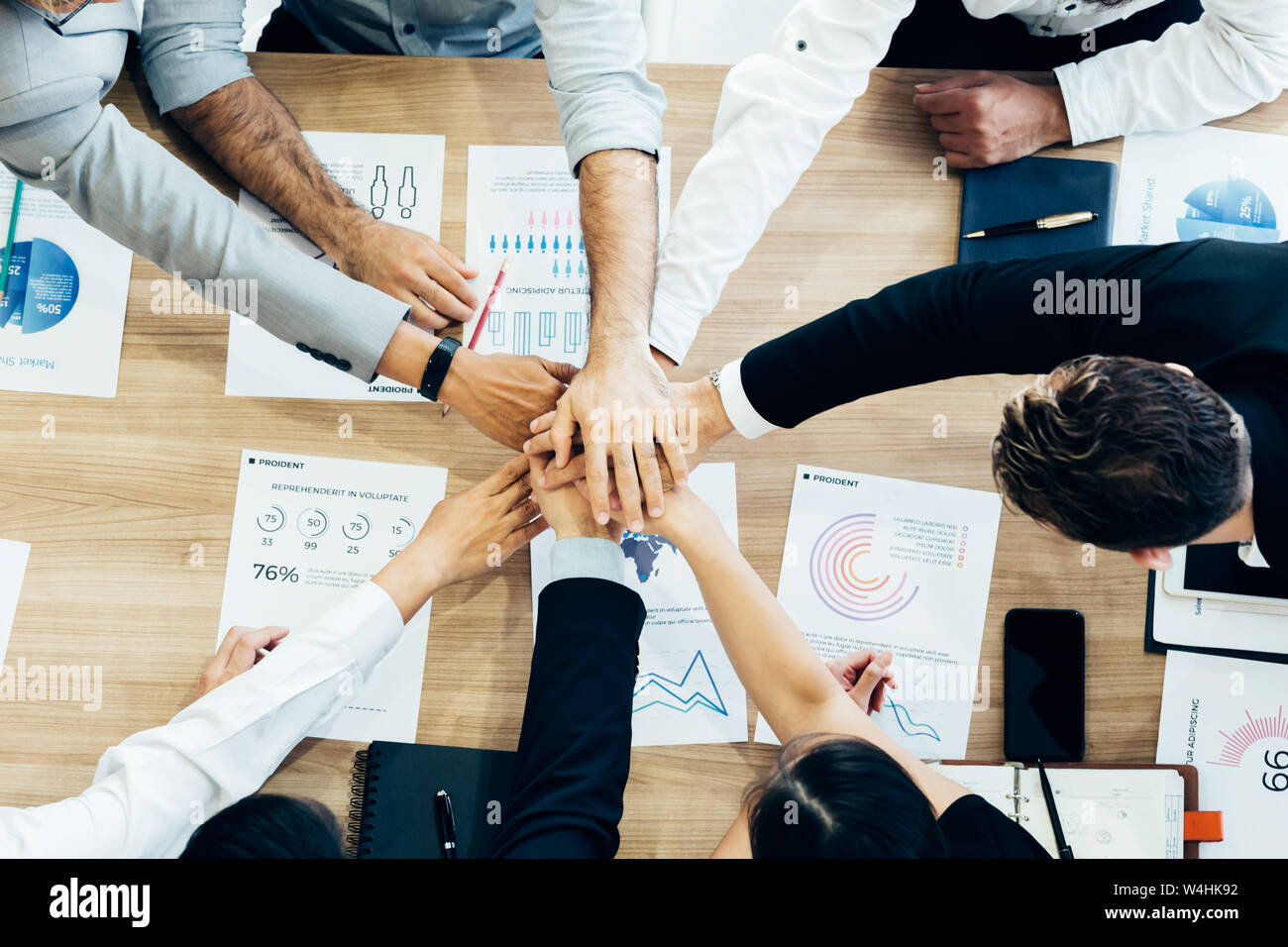 Crop coworking business people stacking hands above wooden desk with paper documents Stock Photo