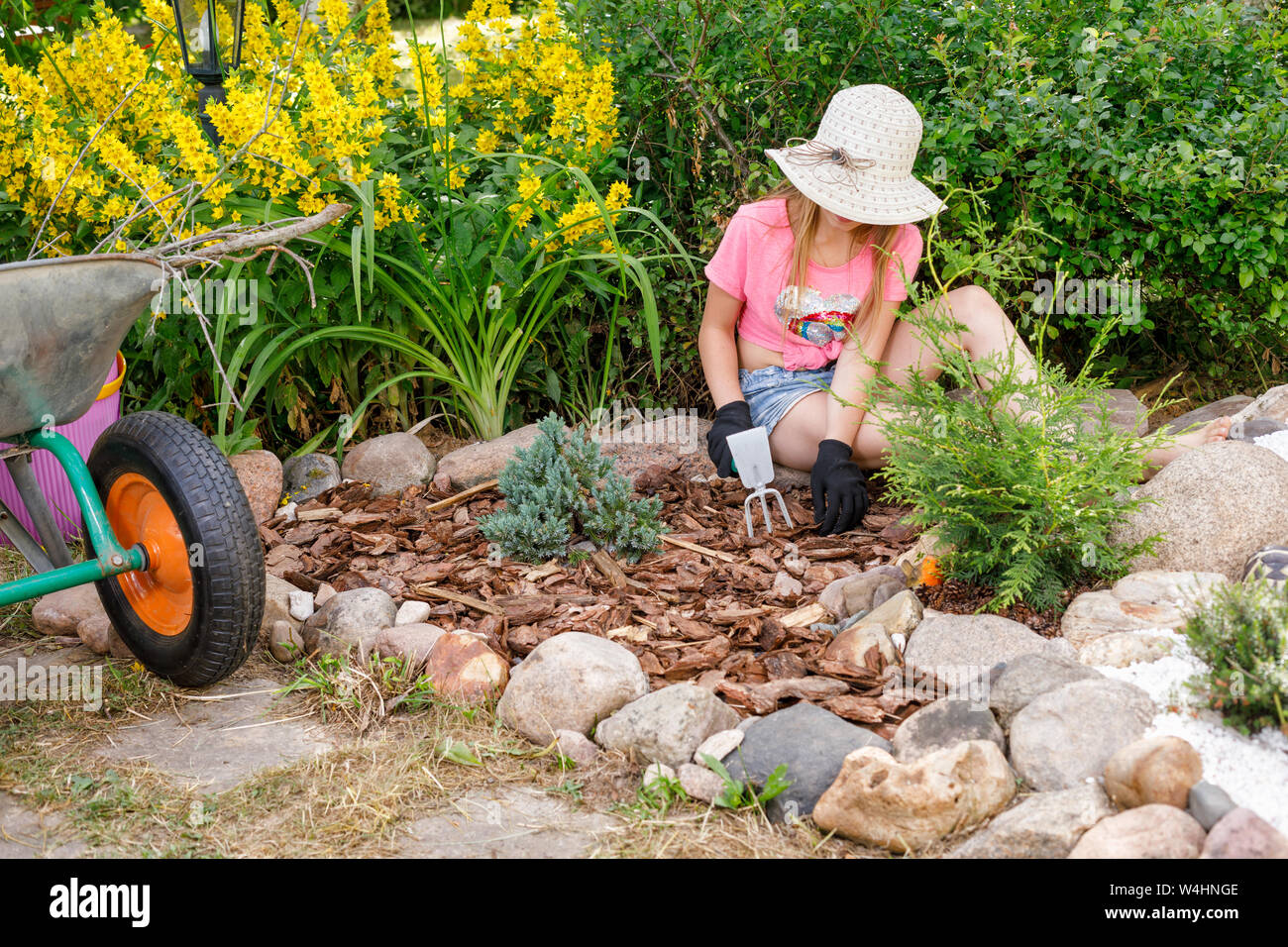 Little girl helping parents in a summer garden cultivating alpine rock garden learning to do gardening work Stock Photo