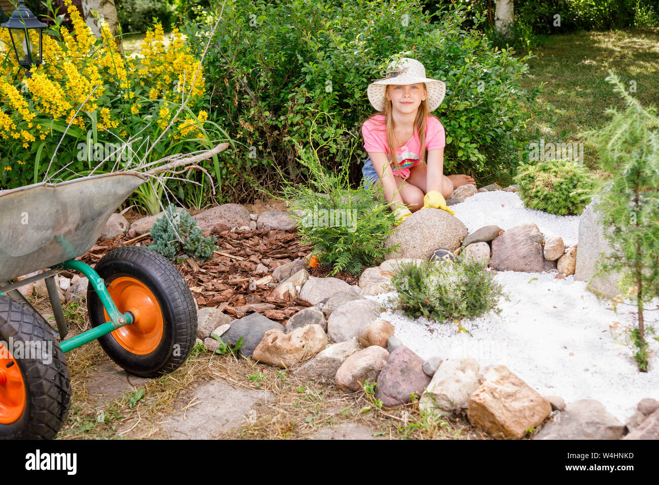 Little girl helping parents in a summer garden cultivating alpine rock garden learning to do gardening work Stock Photo