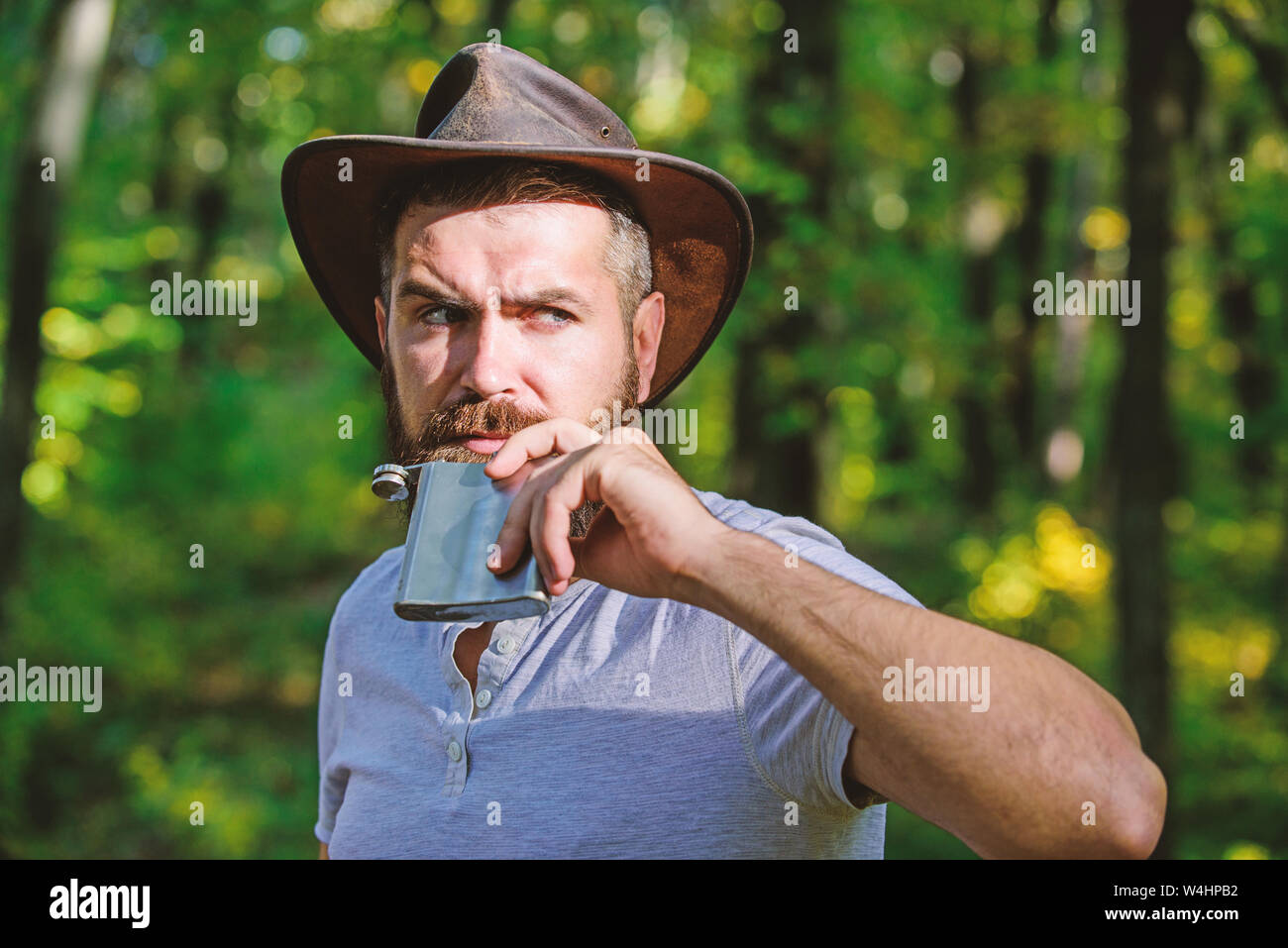 man hipster relax in autumn forest. Spring sunny weather. camping and hiking. mature male with brutal look drink alcohol from metallic flask. Bearded man in cowboy hat walk in park outdoor. Stock Photo