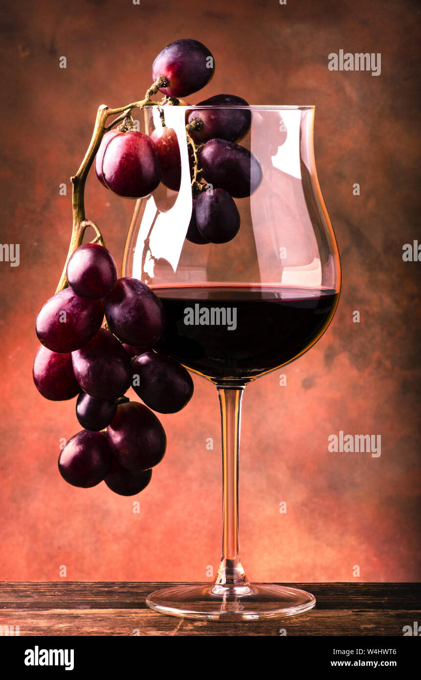 still life. Closeup of a glass with red wine and bunch of grapes on rough wooden table and dark background Stock Photo
