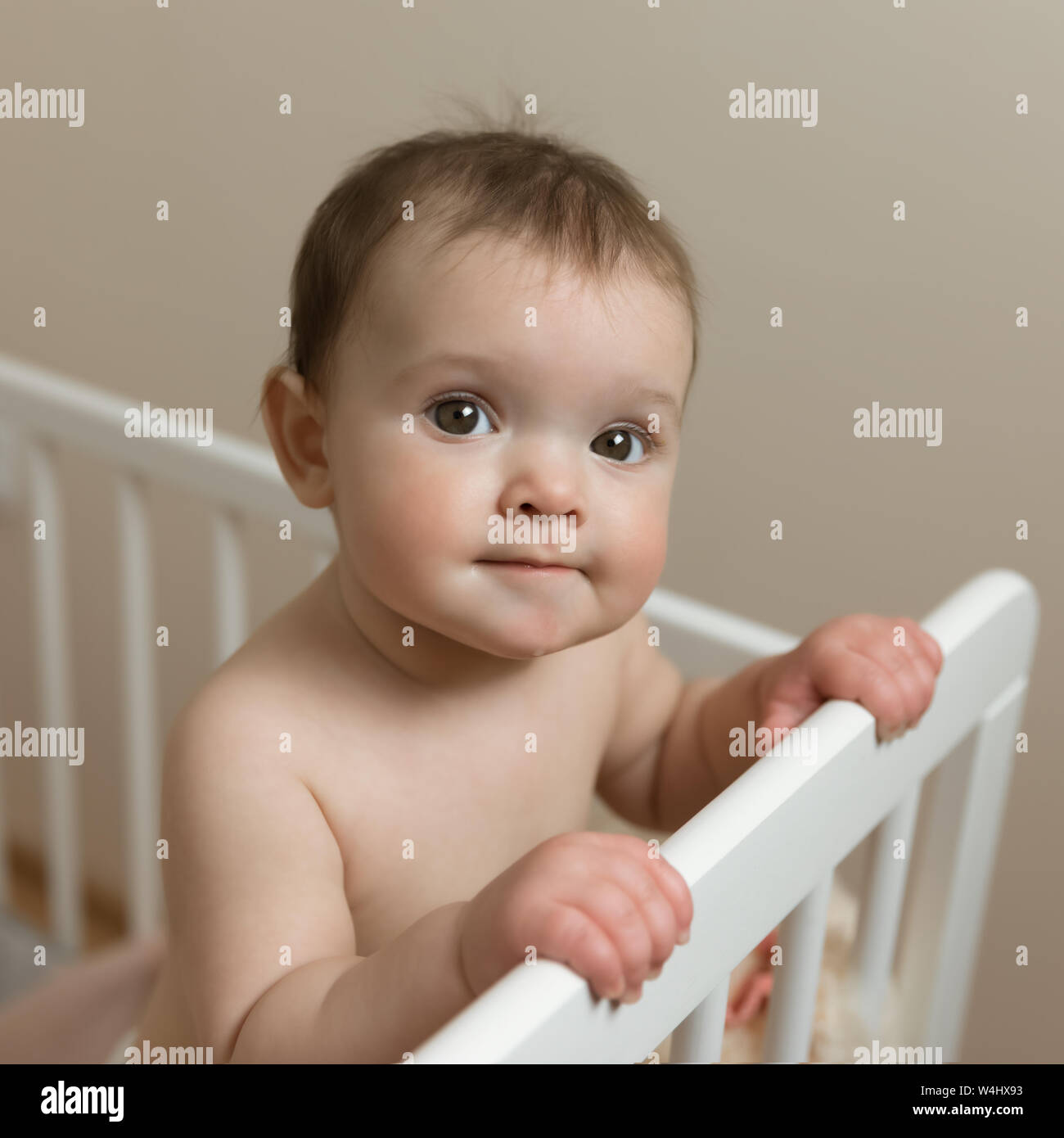 Baby girl in a diaper playing in the crib. Very funny face expression. Stock Photo