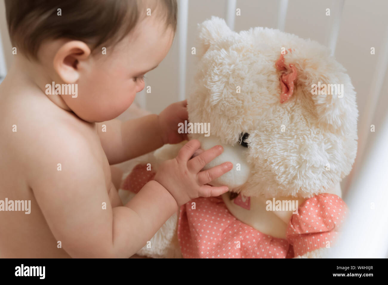 Baby girl playing with a teddy bear in a crib Stock Photo - Alamy