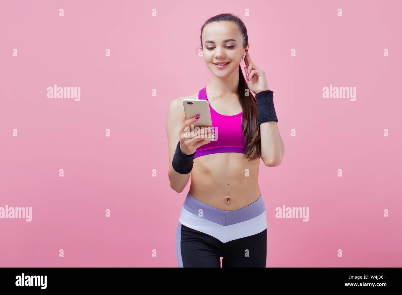Toned young woman stand checking mail on smartphone, fit female athlete in sportswear use mobile phone waiting for training on pink background. Stock Photo