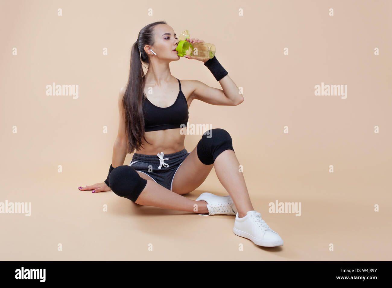 A cute athletic brunette girl, in a tight-fitting sports uniform, sits,  rests after a workout, in black kneecaps, with a bottle for sports  nutrition Stock Photo - Alamy
