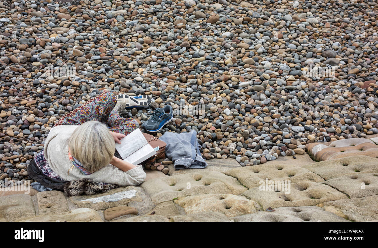 Mature woman reading book on beach.UK Stock Photo