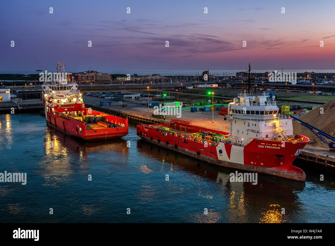 two ships unloading in Zeebrugge docks at sunset. with reflections in the water Stock Photo