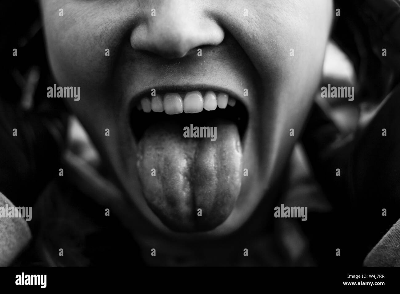 Genre black and white photo. The girl with white teeth and open mouth shows tongue. Cropped photo of a girl's face, without eyes. Stock Photo