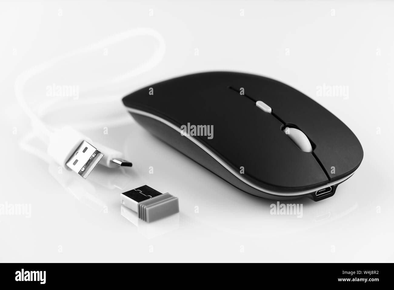 Black wireless computer mouse on a white background. There are a wi-fi adapter and a charging cable. Stock Photo