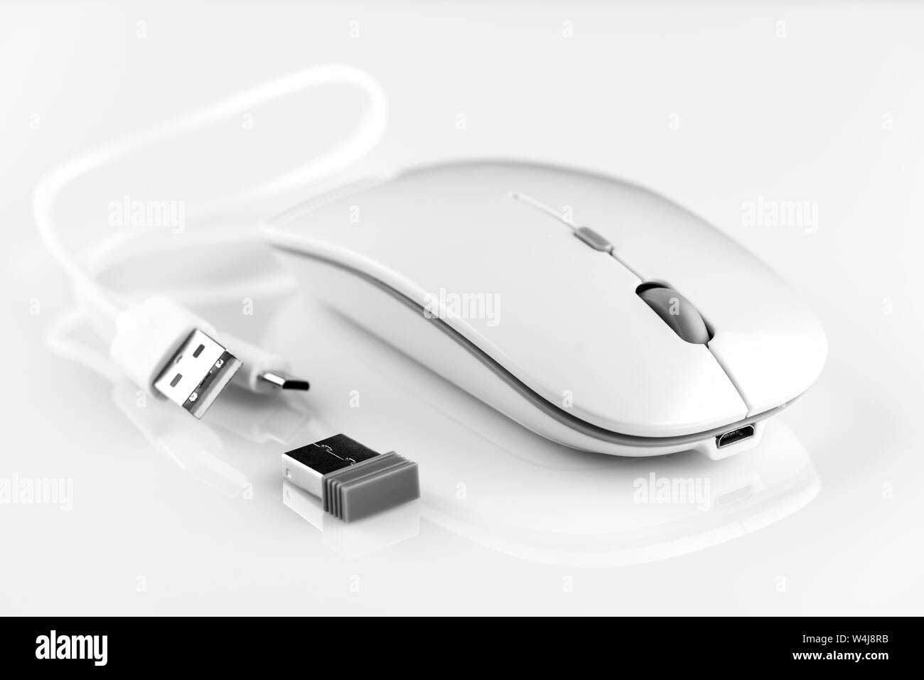 White wireless computer mouse on a white background. There are a wi-fi adapter and a charging cable. Stock Photo