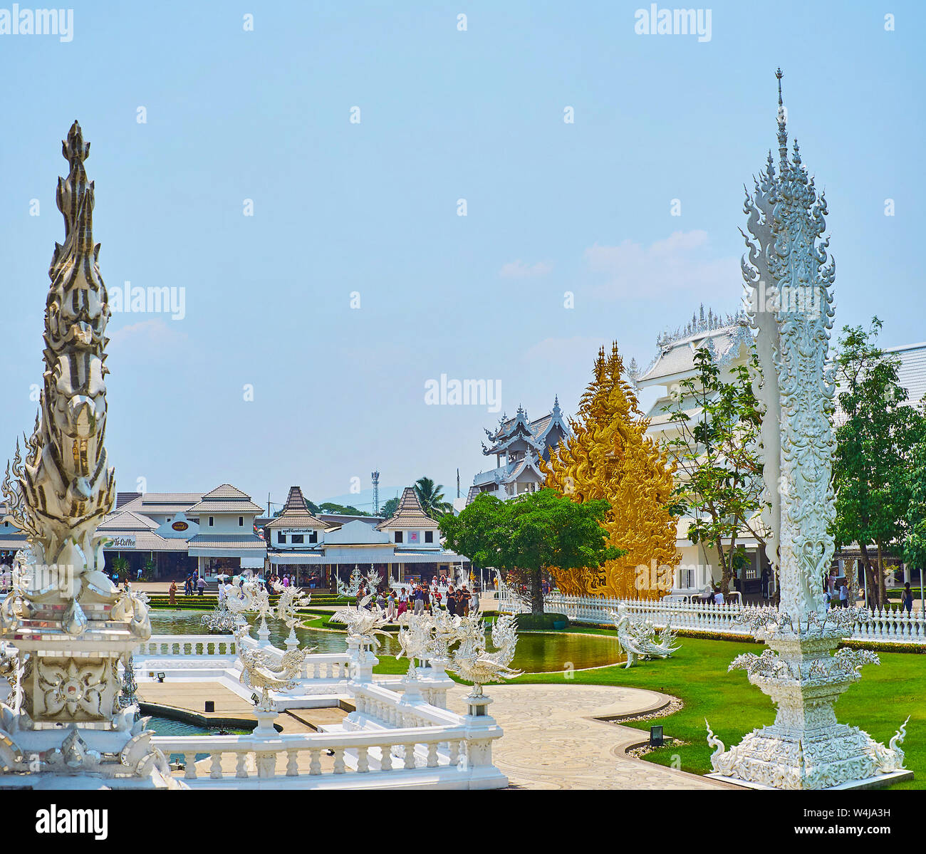 CHIANG RAI, THAILAND - MAY 9, 2019: The scenic territory of White Temple complex with Buddhist pillar, golden shrine, pond with fountains and stucco s Stock Photo