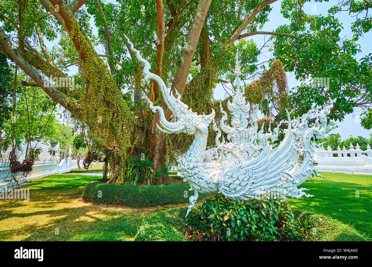 The white stucco statue of mythical half-elephant half-bird creature of hatsadiling (nok hatsadi, nok hat, hatsading) in shade of spreading tree in Wh Stock Photo