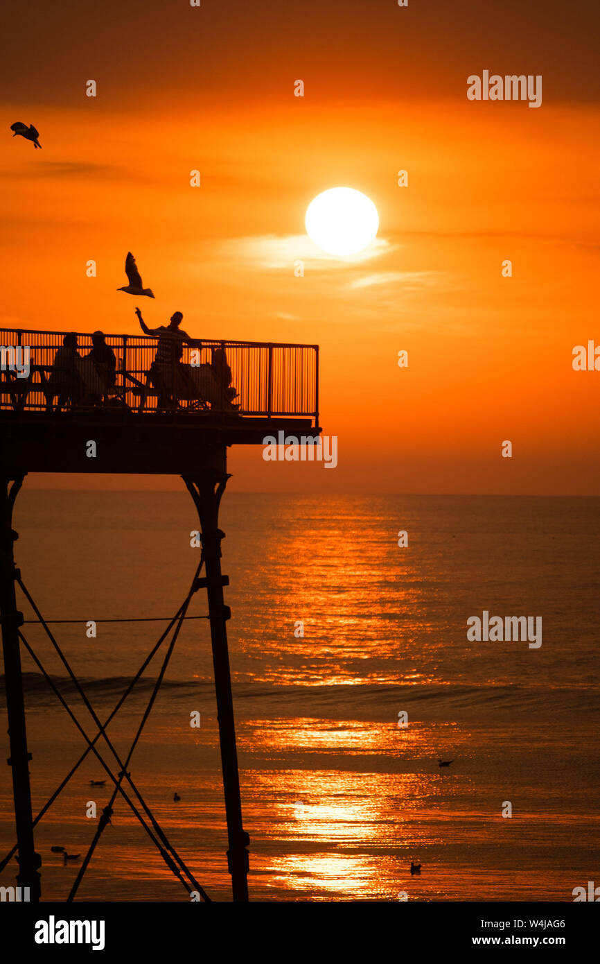 23/07/2019. Aberystwyth, UK.  People on the pier  in Aberystwyth enjoying  a drink at the end of a sweltering summer day of unbroken blue skies and hot sunshine. The country has experienced  the hottest day of the year so far as a plume of scorching hot air drifts in from the continent. Photo credit Keith Morris / Alamy Live News Stock Photo