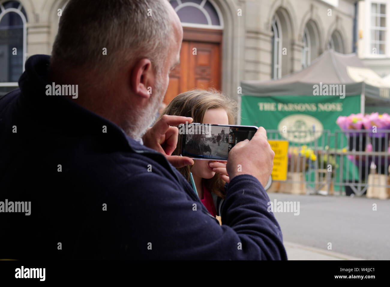 A man is composing a photo on his smartphone of his daughter with Wells Market in the background Stock Photo