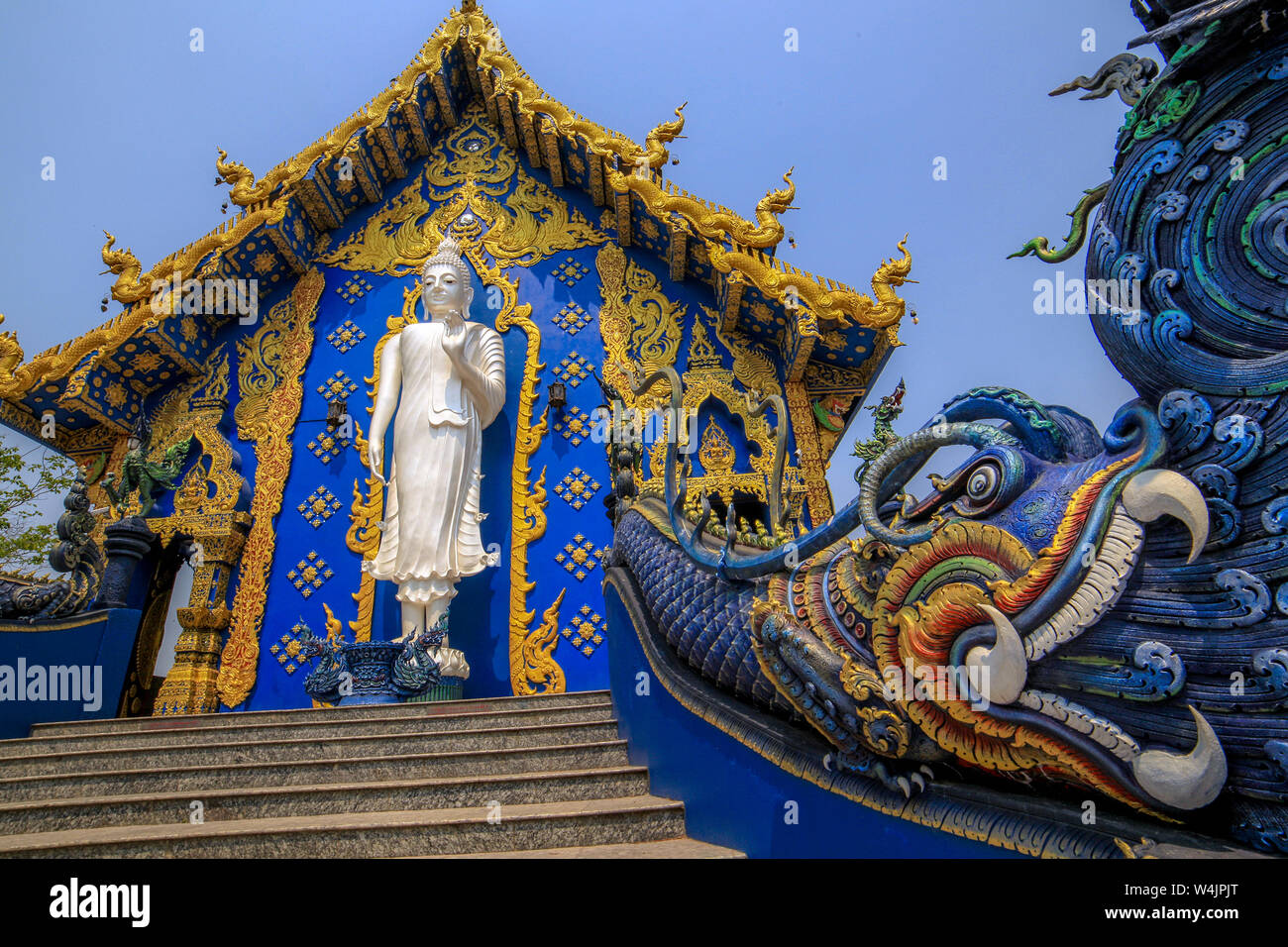 Standing white Buddha statue with a dragon in front of a minor temple at the Wat rong Seua Ten, Blue Temple, near Chiang Rai, Northern Thailand. Stock Photo