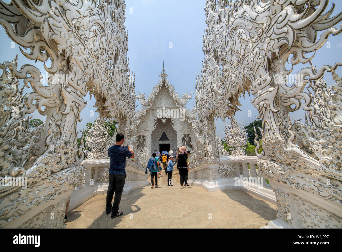 Tourists enter Wat Rong Khun, the White Temple, over The bridge of 'the cycle of rebirth' in Chiang Rai, Thailand. Stock Photo
