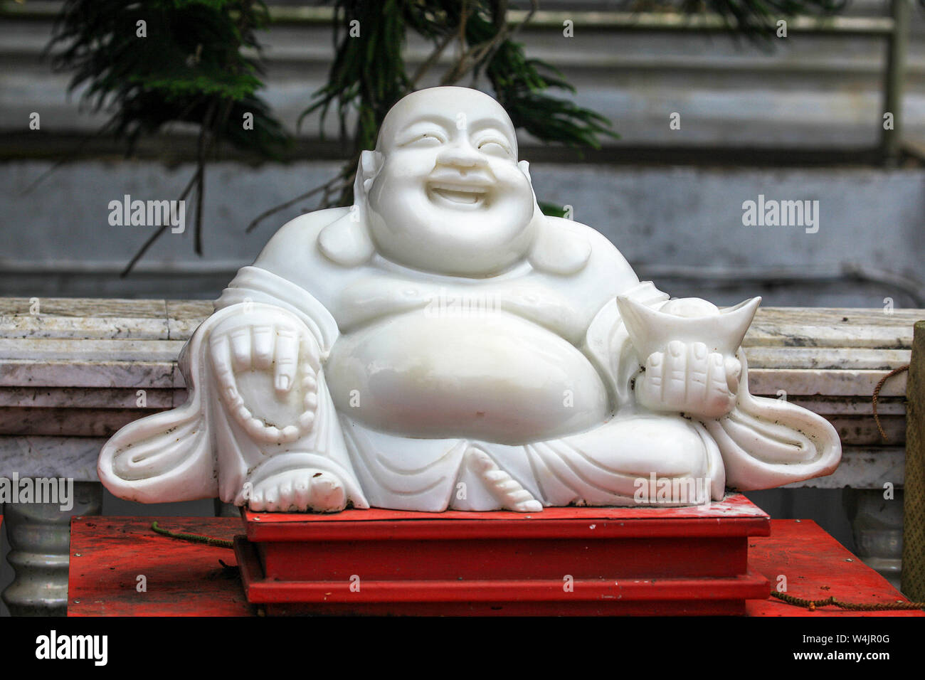 A white statue of Mudai, The Laughing Buddha, sits on a red platform at a temple or wat in Chiang Mai, Northern Thailand. Stock Photo
