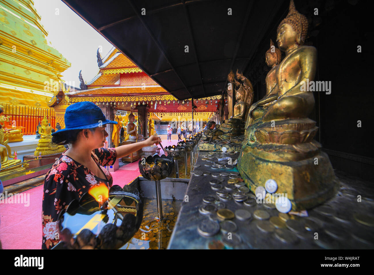 An Asian woman tourist lights votive candles before statues of Buddha at the Wat Phra That Doi Suthep or Doi Suthep for short in Chaing Mai, Thailand. Stock Photo