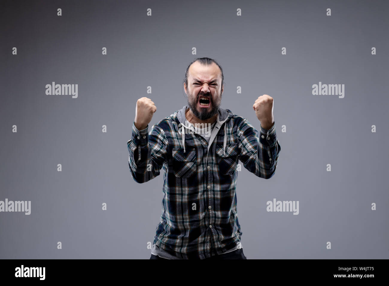 Angry man yelling and shaking his fists at the camera with a furious expression and snarl isolated on grey with copy space Stock Photo