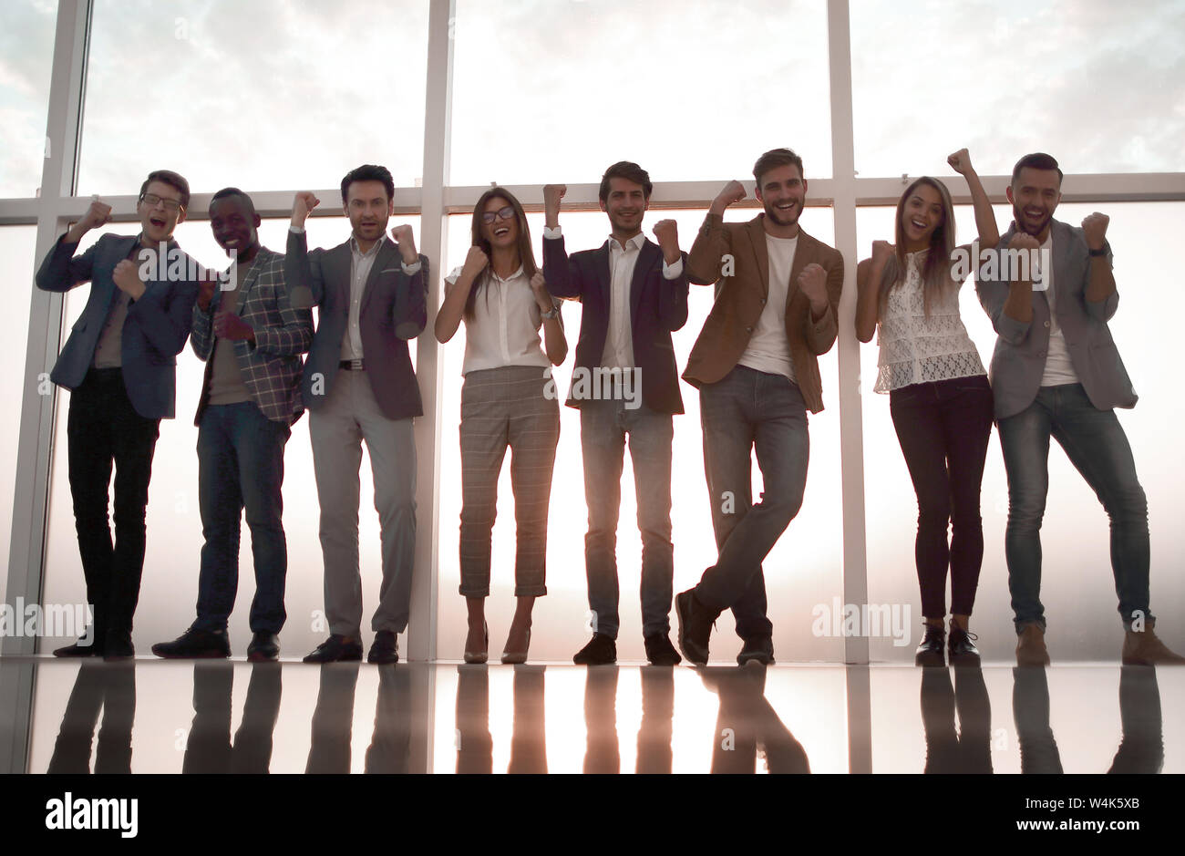 group of young professionals standing in an office with a large window ...