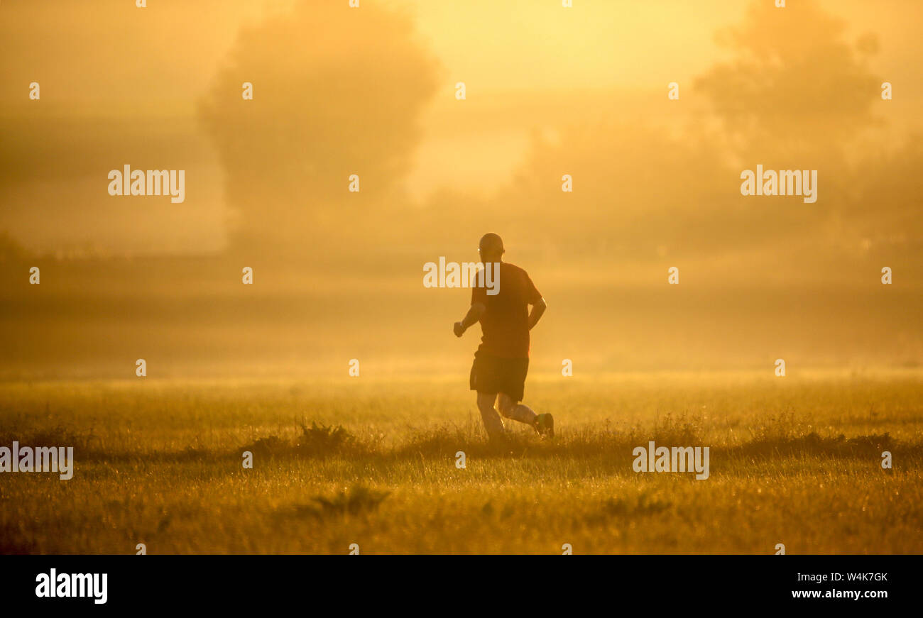 Unlingen, Germany. 24th July, 2019. A jogger runs towards the sun shortly after sunrise. Temperatures of up to 38 degrees are predicted for the course of the day. Credit: Thomas Warnack/dpa/Alamy Live News Stock Photo
