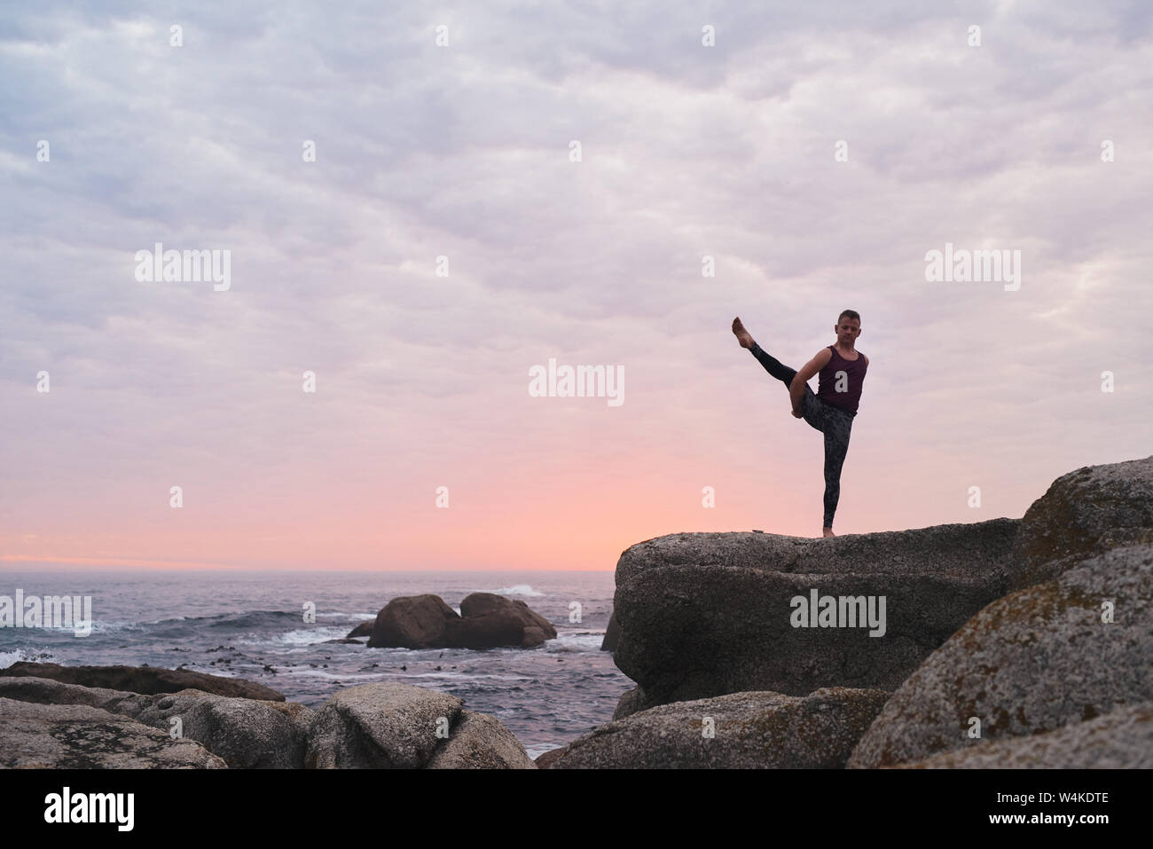Man doing the bird of paradise pose by the ocean Stock Photo