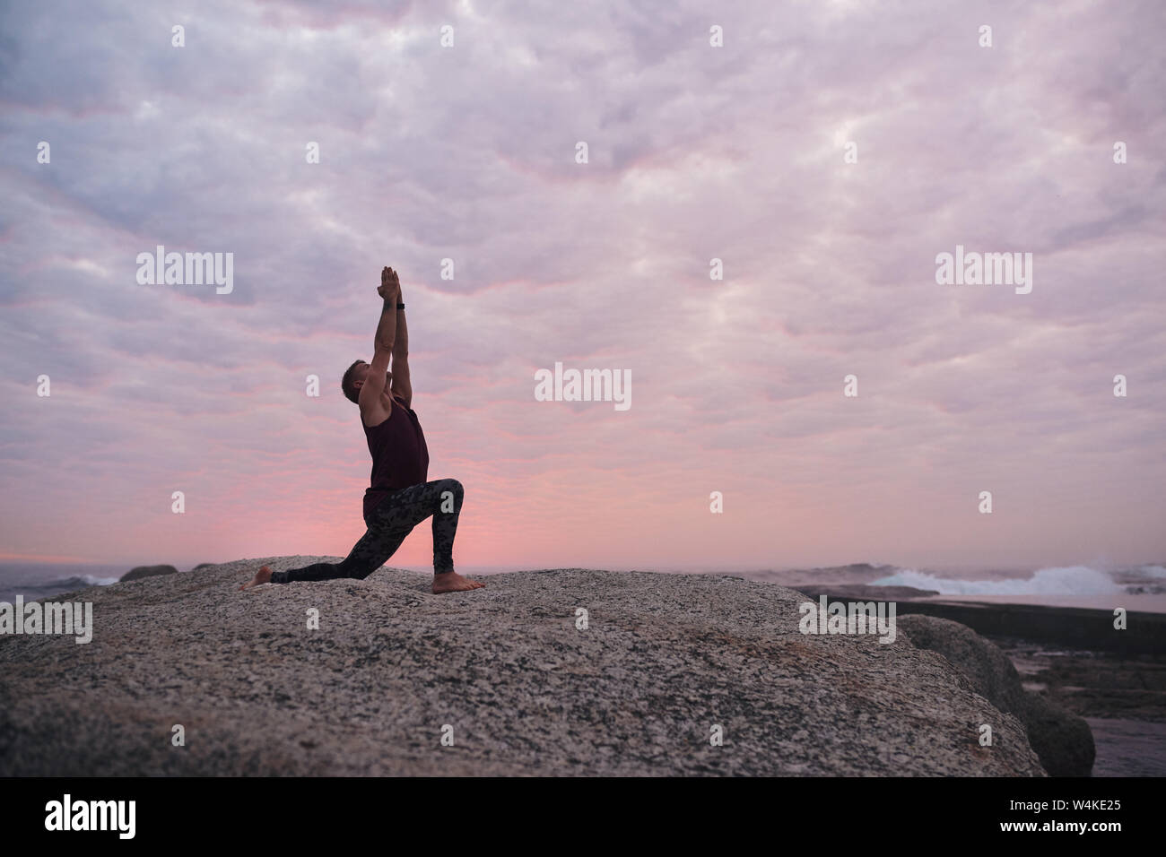 Man doing the cresent lunge pose by the ocean Stock Photo