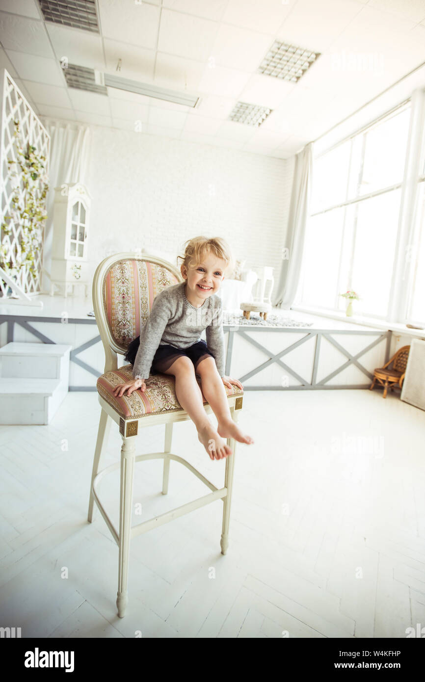 happy five year old girl sitting on a chair in the spacious living room ...