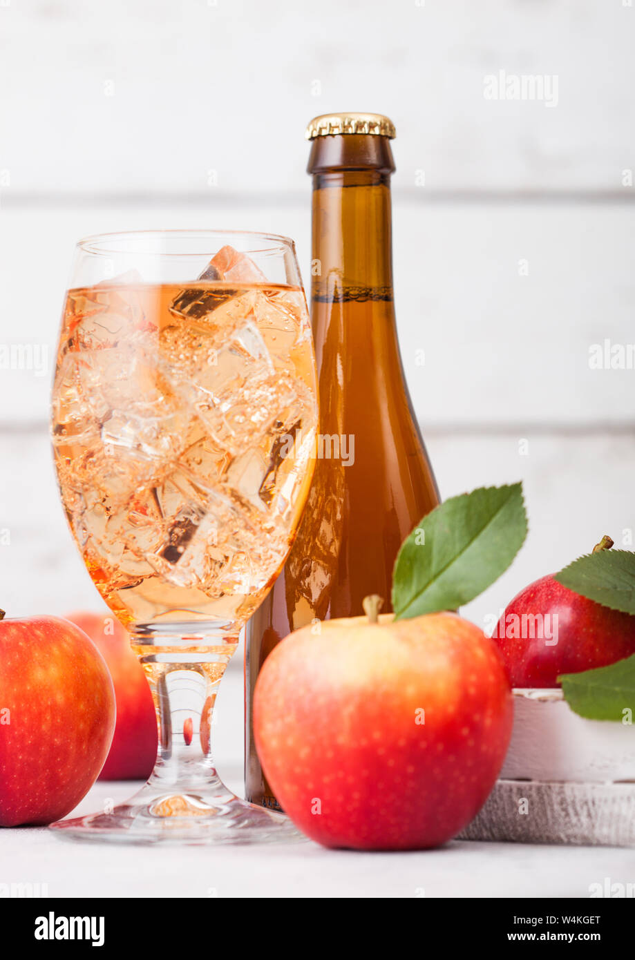 Bottle and glass of homemade organic apple cider with fresh apples in box on wooden background, Glass with ice cubes Stock Photo
