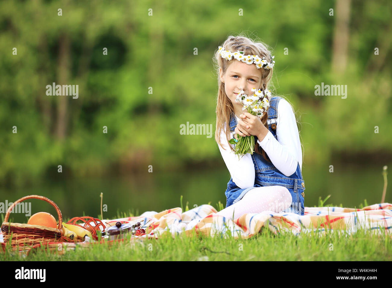 cute little girl in a wreath and a bouquet of wildflowers on a picnic ...